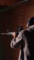 Vertical Shooting gallery client using assault rifle to hit targets, wearing protection headset. Person wearing safety earmuffs at firing range shooting bullseyes, enjoying using semiautomatic weapon video