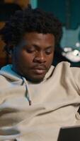 Vertical Black man does his research by reading articles and taking notes at home, collecting information for a new project. Freelancer multitasking and studying files with data driven papers. Camera A. video
