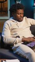 Vertical Adult man typing on a computer at his stylish illuminated apartment, engaging in online work, multitasking efficiently and embracing the flexibility of remote work in a cozy home setting. Camera B. video