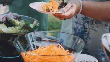 A woman is holding a bowl of carrots at a buffet video