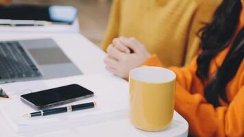 A woman sitting at a desk with a laptop and a yellow mug video