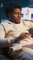 Vertical Positive african american man multitasking on a laptop in stylish loft, fully connected to the internet while managing his freelance work and remote responsibilities. Browsing web at home. Camera B. video