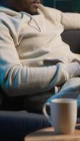 Vertical African american person navigating the internet on laptop at his modern luxury loft, relaxing on the couch and browsing web. Cheerful man does freelance work from home. Camera A. video