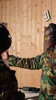 Vertical Portrait of joyous army soldiers wearing safety gear in shooting gallery, preparing to fire at targets. Smiling military units in uniform and protection equipment testing accuracy, camera A video