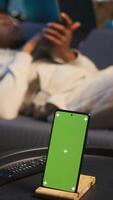 Vertical Black male remote worker laying on the couch next to chroma key display, enjoying leisure and free time for relaxation in his modern loft apartment with neon lights and a smart tv. Camera B. video