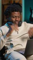 Vertical Freelancer listening to a podcast and being focused on online work, putting on headphones while seated on the couch in his living room. Productivity in a casual and flexible home. Camera A. video