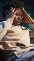 Vertical Black person having health problems suffering from headache and nausea, sitting in the living room and struggling to work on tasks. Remote worker suffering from illness at home. Camera B. video