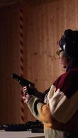 Vertical Person wearing safety equipment loading bullets cartridge in pistol during firearm practice session at shooting range. Woman reloading gun, pointing weapon at targets, learning self defense, camera A video