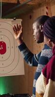 Vertical Shooting gallery instructor explaining bullseye scoring system to customers. African american firing range specialist teaching clients bullseye points system, discussing industry regulations, camera A video