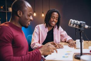 Podcasters discussing data visualizations during collaborative recording session in contemporary broadcasting workspace photo