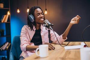 Radio host engaging with a microphone while recording a podcast in a modern home studio, surrounded by audio equipment and books photo