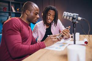 Podcasters recording episode, referencing smartphone, browsing social media, engaging with follower comments during live broadcast photo