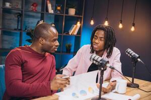 African American podcast team reviewing data graphs while recording in soundproof professional studio setting photo
