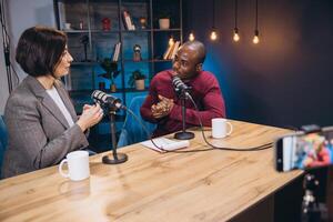 Podcasters discussing topics while sitting at professional recording studio, microphones, soundboard, and sleek interior visible in background photo
