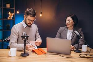 Professional podcasters collaborating, using laptop while recording audio episode in soundproofed studio, capturing conversational moment photo