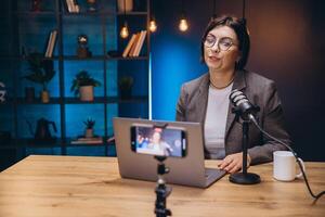 Female content creator recording podcast interview using professional microphone and smartphone at home workspace photo