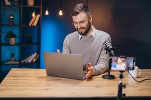 Happy podcaster gesturing and speaking during a podcast and streaming session using laptop, microphone and smartphone photo