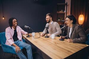 Professional podcast team recording, smiling while speaking into microphones inside soundproof studio setting, capturing audio content photo