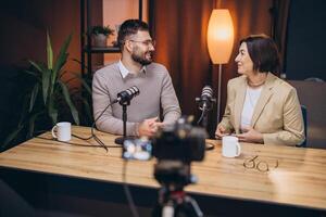 Two podcasters sitting at a table, recording a new episode in a professional studio, using microphones and a camera photo