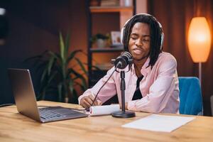 African American man content creator recording a podcast at home, using a microphone and headphones while engaging in lively discussions and sharing insights photo