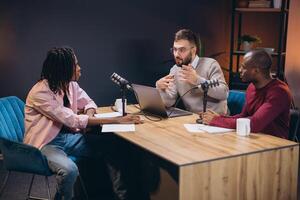 Podcasters discussing animatedly while recording in professional studio, surrounded by microphones, sound boards, and high tech recording gear photo