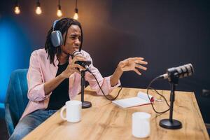 African American Professional radio host speaking passionately into microphone, gesturing dynamically during podcast recording in soundproof studio environment photo