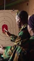 Vertical Army commander teaching recruits in shooting gallery how to shoot paper targets, explaining pointing system. Military officer instructing soldiers on how to hit bullseye, reading rules, camera A video