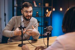 Two podcasters engaging in a lively conversation while recording a new episode in a professional studio filled with advanced equipment photo