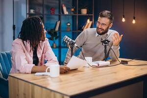 Podcasters recording episode, discussing content with microphones, notes spread across workspace, capturing dynamic conversation photo