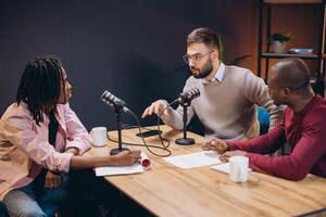 Three radio hosts interviewing a guest in a professional recording studio, discussing and sharing ideas during a podcast episode creation photo