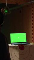 Vertical Green screen laptop next to shooting gallery safety officer watching client shoot at targets, supervising him. Mockup notebook and firing range expert teaching man how to use firearms, camera A video