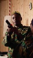 Vertical Army commander talking with recruits in shooting gallery, showing them how to reload firearms. Military officer instructing soldiers on how to load ammunition into pistol, camera A video