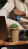 Vertical African american male person listening to a podcast and multitasking on the coffee table, browsing the internet and navigating through his laptop with headphones on. Self employed man. Camera A. video
