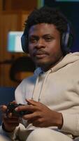 Vertical African american guy in modern apartment plays games competition, relaxing and having fun. Person in multiplayer game on gaming console during leisure time at home. Camera A. video