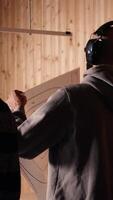 Vertical Man in firing range doing shooting sport, looking at results on paper target. Person wearing safety gear training with handgun, sharpening skills, checking points scored on bullseye, camera A video