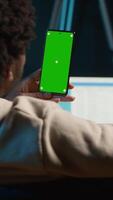 Vertical Confident tech user looking at isolated mockup display in his living room, relaxing with his remote job on the couch. African american happy adult browses the internet. Camera A. video