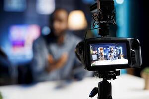 African american content creator in blurry background filming tech reviews for his internet channel, using professional production gear in foreground capturing footage photo