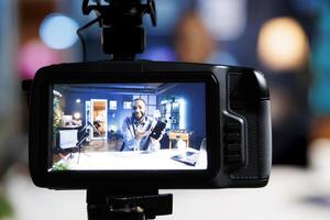 Focus on professional production camera used for capturing footage of tech engineer in blurry background filming newly launched smartphone review for online audience, showcasing mobile phone photo
