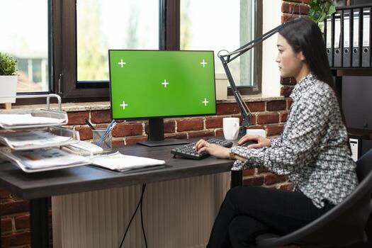 Professional woman examining business plans at office desk, utilizing desktop pc with blank template display in startup workspace. Focused manager working on computer with isolated chromakey template. photo