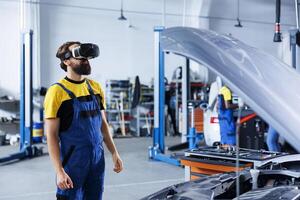 Engineer in auto repair shop using virtual reality goggles to visualize car battery in order to fix it. Trained garage worker wearing futuristic vr headset while working on broken vehicle photo
