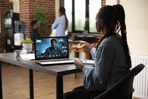 Black woman uses laptop to collaborate remotely, discussing project plans with coworker in virtual meeting. Female advisor at desk engaging in call with male client to share marketing strategies photo