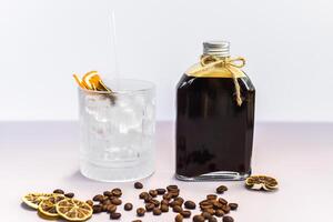 Cold brew coffee in a bottle with transparent glass full of ice on light gray background side view photo
