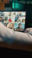 Vertical Focused young man smiling and waving during a web conference at his home, showcasing online communication in a digital and wireless lifestyle. Conference speaker with attendees. Camera A. video