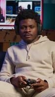 Vertical African american man plays intense online games at home, spamming attack buttons on his controller. Gamer participating in online competition, playing on gaming console. Camera A. video
