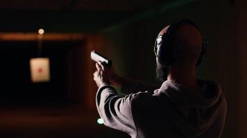 Shooting gallery customer using pistol to hit targets, wearing protection headset. Person wearing safety earmuffs at firing range shooting bullseyes, enjoying using weapon video