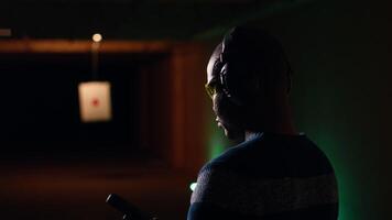 Portrait of smiling man doing training in shooting range, learning proper pistol holding etiquette and having fun. Cheerful gun hobbyist practicing with weapons, wearing protective eyewear, camera B video