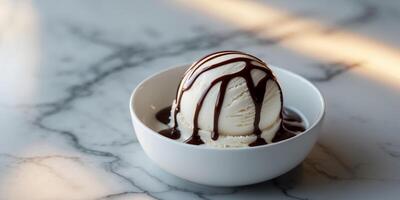 Ice cream in a white bowl drizzled with chocolate syrup on a marble table with soft natural lighting Copy Space. photo