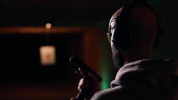 Shooting range customer shooting targets with pistol, learning to operate handgun in close quarters. Man at indoor shooting ground firing lethal fire weapon, wearing protection equipment, camera B video