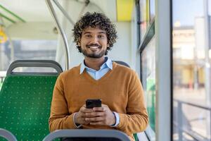 A man uses an app on his smartphone while riding public transport, smiling and looking at the camera with the phone in his hands. photo