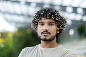 Close-up portrait of a young calm and serious man, looking at the camera, walking outside in the park. photo